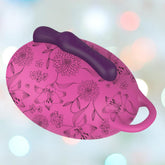 A pink flower-patterned round hairbrush with purple bristles and handle, in front of a blurred pastel bokeh background, echoes the playful elegance of the Bouncy Bliss Seat Vibrator with 10 Vibration Modes.